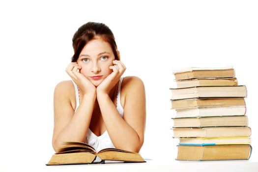 Young pretty caucasian girl holding her head, sitting near the pile of books and thinking.