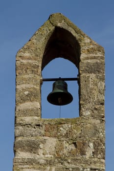 Stone built bell tower with bronze bell, swing bar and rope with ringer.