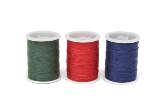 Three spools of thread of various colors, green, red and blue, isolated on white background