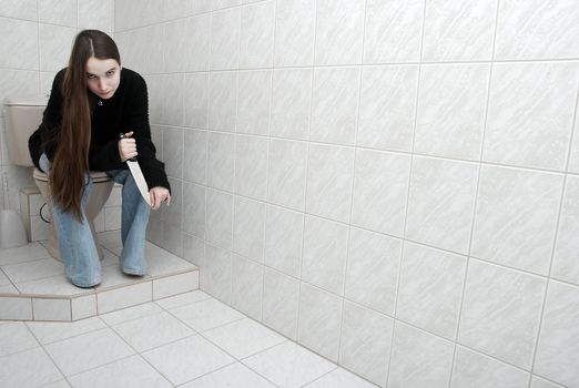 Girl sitting in the bathroom with knife in hand