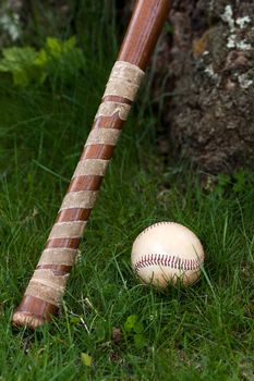 An old wooden baseball bat and ball laying in the green grass with copyspace.  Shallow depth of field.