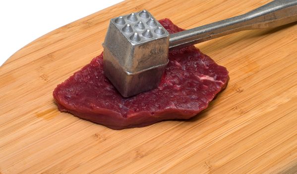 Piece of beef and a kitchen mallet on a wooden cutting board.