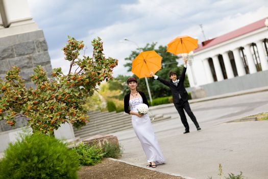 laughing  bride and groom with orange umbrellas 