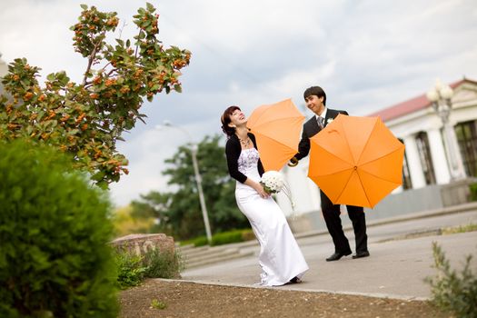 laughing  bride and groom with orange umbrellas 