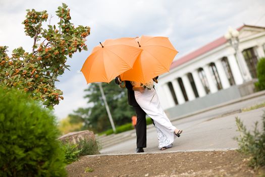 bride and groom closing faces with orange umbrellas 