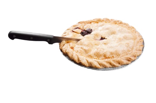 Cherry pie in a dish with a knife preparing to cut a slice out of it, isolated on white