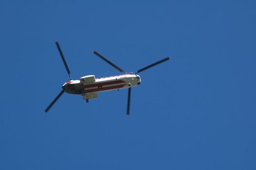 A twin rotor helicopter flying overhead against a blue sky