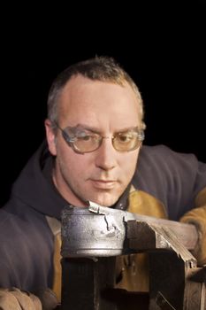 closeup of a blacksmith at work, studying his work as he bends it around a form