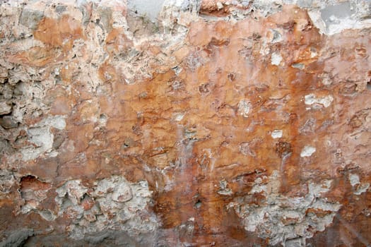 weather-beaten wall made of clay and stones with holes and flaking surface