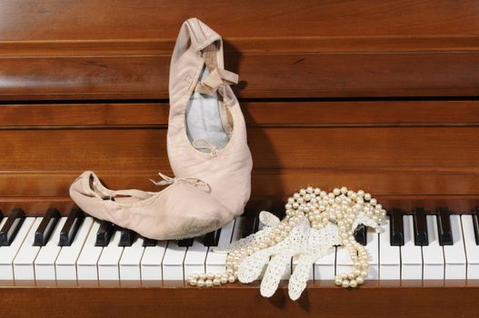 Lace glove, ballet shoes and pearls sitting on piano keys