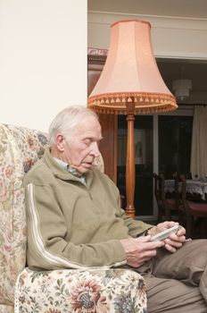 Elderly man sitting in an armchair using TV remote 