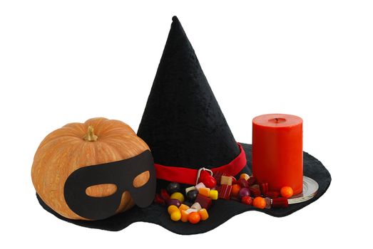 Halloween candies, burning orange candle and masqueraded pumpkin on edge of black witch hat isolated on white background