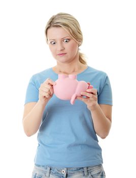 Young blond woman trying to get money from her piggy bank, isolated on white background
