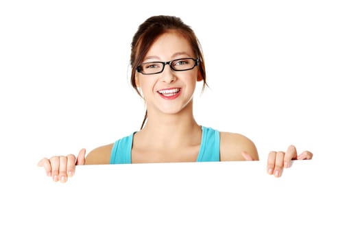 Young caucasian smiling girl in glasses holding white sheet of paper over white background