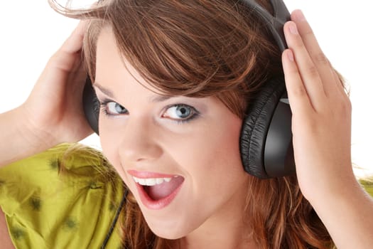 Beautiful teenage girl in a green dress listening to music with big headphones, isolated on white