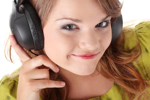 Beautiful teenage girl in a green dress listening to music with big headphones, isolated on white