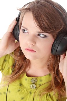 Beautiful teenage girl in a green dress listening to music with big headphones, isolated on white