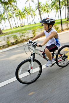 Young Asian boy cycling in a greenery park.