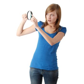 Young attractive smiling teen woman looking into a magnifying glass, isolated