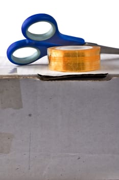 Tape with scissors on worn-out cardboard box isolated on white