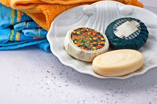 Three bath soaps with towels in the background and droplets