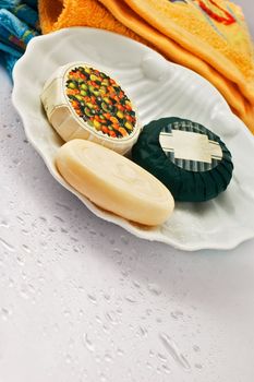 Three bath soaps with towels in the background and droplets