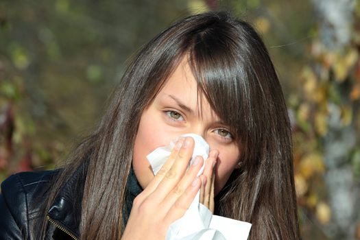Teen Girl blowing her nose outdoors in late autumn.