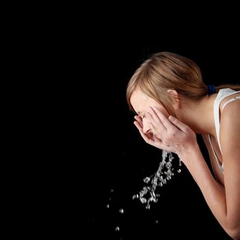 Teen girl washing her face with water, isolated on black