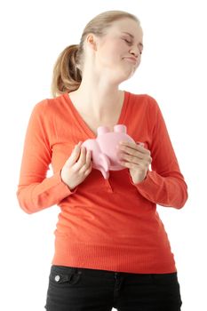 Young blond woman trying to get money from her piggy bank, isolated on white background