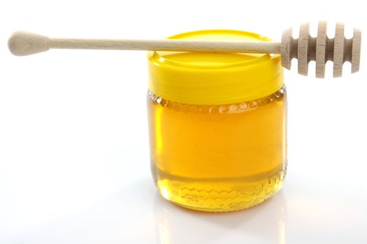 Wooden honey drizzler on honey jar isolated on white.