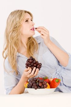 A pretty woman with bowl of fruit lying in the arm and eats a grape