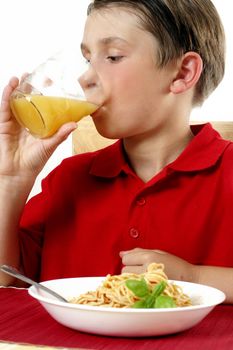 A child drinking orange juice from a plastic cup.  He is sitting at the dinner table.  Focus on boy with juice.