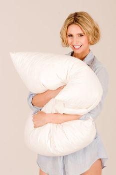 Young smiling blond girl cuddling with a pillow