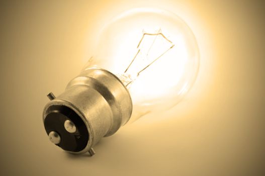 Close up of a single illuminated light bulb with warm golden background