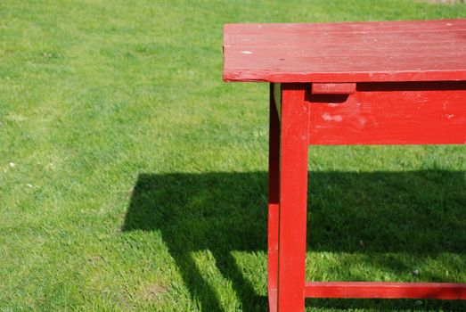 Self made table of planks coloured red standing on the green grass