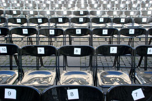 Black plastic chairs set for an outdoor event with numbers on back