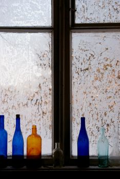 Window covered in rime. There are some coloured bottles on the sill.