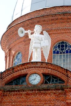 White angel with trumpet and book in hands on red bricks building