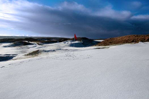red flag on a snow covered links golf course in ireland in stormy winter weather
