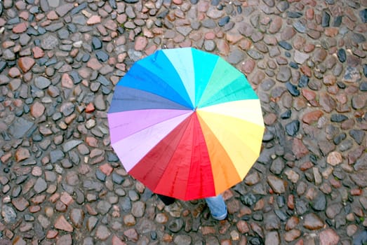 Rainbow-colored umbrella even in heavy day illuminates pavement of the old downtown