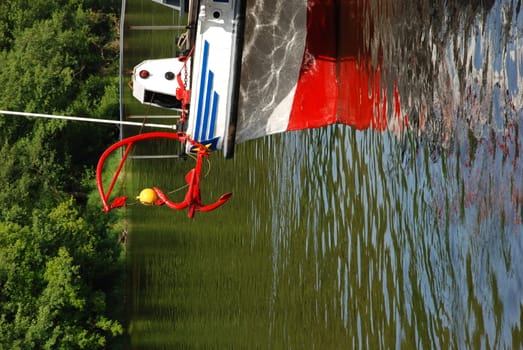 Travel ship fragment with reflections on the river and red anchor