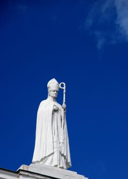 Religious-themed statue of pope with the stick against the sky.