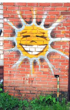Graffiti of cheerful smiling sun on the red brick wall