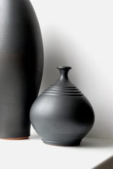 Black pottery vases on a windowsill in a white background
