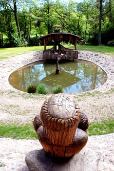 Round cobbly stoned pond with wooden sculptures near it