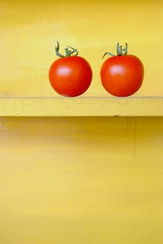Two red tomatoes in yellow wooden shelf.
