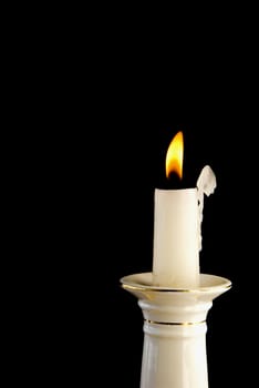 White burning candle in candlestick in the dark background