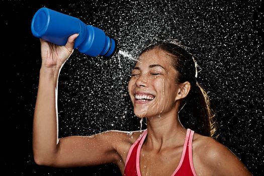 Woman fitness runner drinking and splashing water in her face. Funny image of beautiful female fitness model on black background.