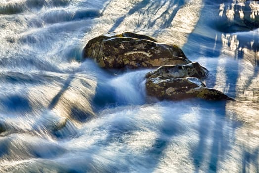Sunlight illuminates rocks in middle of raging flooded river in Smoky Mountains