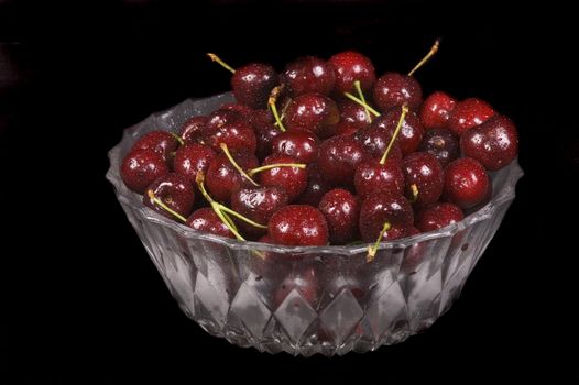 Glass bowl of fresh cherries on  black background
